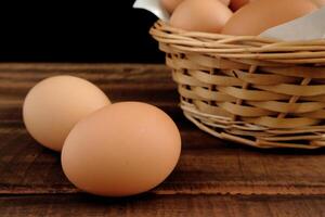 Fresh chicken eggs and egg carton on old dark brown wooden table in front of black background photo