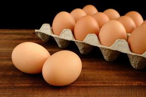 Fresh chicken eggs and egg carton on old dark brown wooden table in front of black background photo