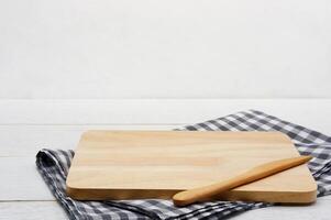 Empty rectangle wooden serving board with butter knife and grey gingham tablecloth on white wooden table. photo