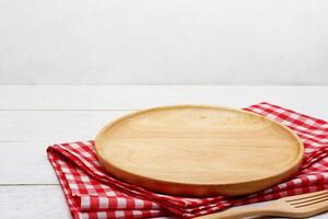 Empty round wooden plate with fork and red gingham tablecloth on white wooden table. photo