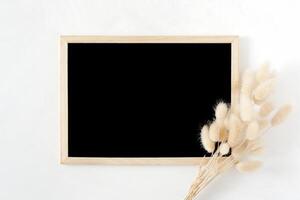 Blank wooden chalk board with natural dried hare's tail grass bouquet on white background. Top view image. Feminine styled stock photography for blog posts and social media content. photo