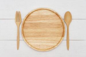 Empty round wooden plate with spoon and fork on white wooden table. Top view image. photo