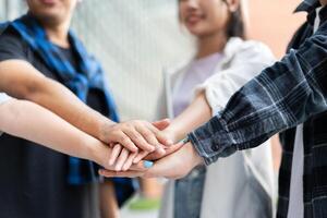 Group of cheerful young Asian entrepreneurs joining hands together to celebrate, excited success for achievements obtained. Undergraduate students celebrate success after end project, teamwork concept photo