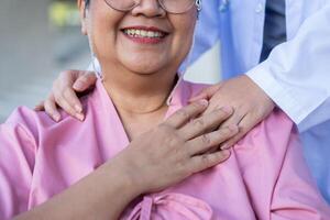 Asian careful caregiver or nurse hold the patient hand and encourage the patient in a wheelchair.  Concept of happy retirement with care from a caregiver and Savings and senior health insurance. photo