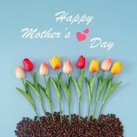 Creative composition made with colorful spring tulip flowers and roasted coffee beans on blue background with Happy Mother's Day text. Minimal Mothers Day concept. Nature flat lay. Top of view. photo