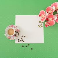 Creative spring layout of coffee cup, coffee beans, beautiful orchid flower and paper card note copy space on green background. Minimal concept. Trendy coffee with flowers idea. Spring flat lay. photo