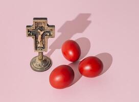 creativo diseño hecho con cristiano santo cruzar y rojo de colores Pascua de Resurrección huevos en ligero rosado antecedentes. mínimo Pascua de Resurrección concepto. Pascua de Resurrección fiesta composición idea. foto