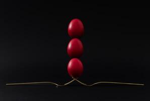 Creative Easter holiday composition made with red colored eggs balancing on golden forks against black background. Minimal Easter concept. photo