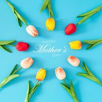 Creative spring composition made with colorful tulip flowers with Happy Mother's day text on blue background. Minimal Mothers day concept. Trendy spring flowers idea. Nature flat lay. photo