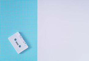 Layout of retro white audio cassette tape on white and blue background. Creative concept of old technology. 80's aesthetic. Vintage audio cassette tape idea. Retro fashion nostalgia. Retro futurism. photo