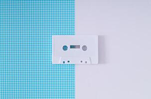 Layout of retro white audio cassette tape on white and blue background. Creative concept of old technology. 80's aesthetic. Vintage audio cassette tape idea. Retro fashion nostalgia. Retro futurism. photo