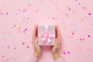 ai generado un mujer manos sostener un regalo en un rojo y rosado pastel mesa desde arriba. eso es un plano laico preparar Perfecto para cumpleaños o bodas foto