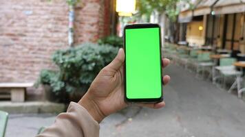 Holding slim telefoon met groen scherm met wazig cafe straat achtergrond. video