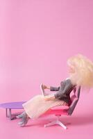 muñeca con ordenador portátil en silla en rosado antecedentes. trabajando a hogar, Lanza libre creativo concepto. foto