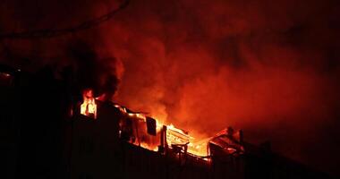 Huge fire blazing in apartment building. Burning house is engulfed in flames at night during the disastrous video