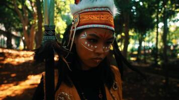 Portrait of a person in traditional indigenous attire with face paint, standing in a forest setting. video