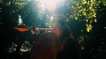 Person in traditional attire with a fan, backlit by sun filtering through trees, creating a moody, ethereal atmosphere. video