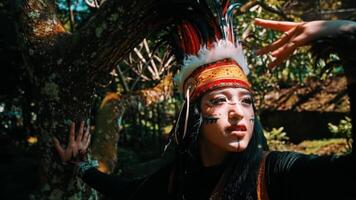 Portrait of a person in traditional ethnic attire with intricate patterns and a feathered headdress, set against a lush green forest backdrop. video