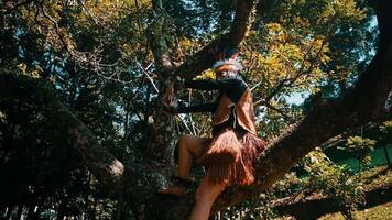 Person in tribal attire posing on a tree in a lush forest setting. video