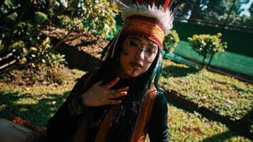 Person in traditional indigenous attire with face paint, holding a drum in a lush forest setting. video