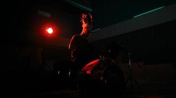 Drummer in silhouette playing on a drum set with a red stage light video