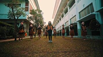 Group of students in uniform walking in school courtyard with masks on, concept of education video