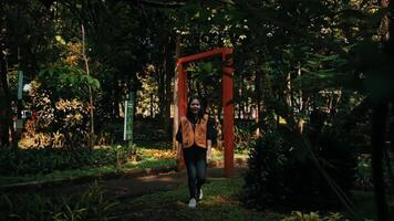 Person standing in a garden with a red frame structure, surrounded by lush greenery and plants. video