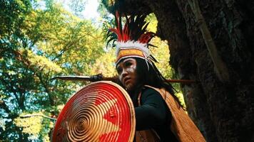 Indigenous person in traditional attire playing a drum in a lush forest setting. video