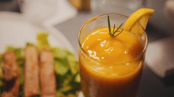 frisch Orange Saft im ein Glas mit ein Scheibe von Orange und Rosmarin, mit ein verschwommen Hintergrund von ein Mahlzeit. video