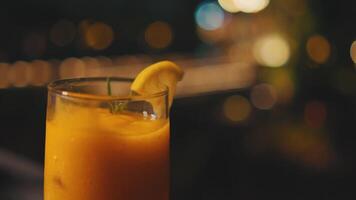 refrescante naranja cóctel con un limón rebanada en el borde, servido en un alto vaso en contra un borroso antecedentes con bokeh luces. video