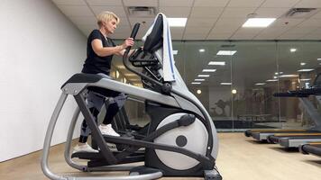 Middle-aged woman goes in for sports on an elliptical exercise machine. video