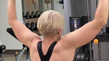 Woman exercise workout on machine in gym. Woman on the exercise machine, rear view. Caucasian woman trains pull-ups on the horizontal bar on a machine in the gym. video