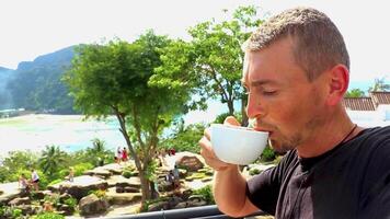 Male tourist man with coffee at beautiful famous beach lagoon panorama view between limestone rocks turquoise water on the viewpoint on Koh Phi Phi Don island in Ao Nang Krabi Thailand. video