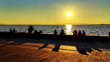 People Watching Seascape and Resting on Wooden Beach at Sunset Silhouette video