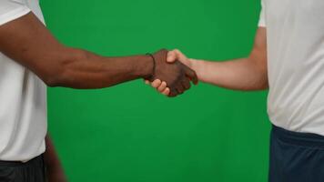 Unrecognizable caucasian and african american sportsmen shaking hands leaving green video