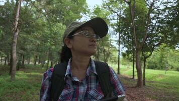 ásia botânico mulher dentro casual vestir com mochila segurando digital tábua e caminhando enquanto examinando silvicultura área dentro público parque. consciência do sustentável de Meio Ambiente problemas. video