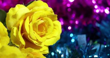 Close-up of artificial yellow rose on top of glittering blue and pink tinsel bokeh background video