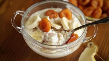 cooked boiled sweet oatmeal with with dried apricots and bananas in a bowl on a wooden table video