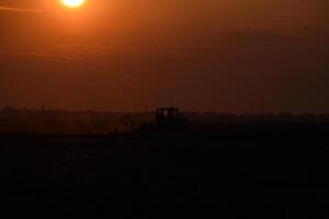 tractor arada arado el campo en un antecedentes puesta de sol. tractor silueta en puesta de sol antecedentes foto