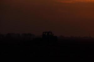 Tractor plowing plow the field on a background sunset. tractor silhouette on sunset background photo