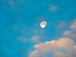 el Luna en el azul cielo con nubes dos cuarteles de el lunar foto