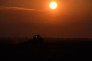 tractor arada arado el campo en un antecedentes puesta de sol. tractor silueta en puesta de sol antecedentes foto