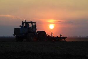 Tractor plowing plow the field on a background sunset. tractor silhouette on sunset background photo