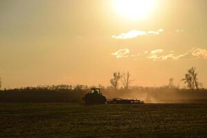 Tractor at sunset plow plow a field. Tilling the soil in the fall after harvest. The end of the season photo