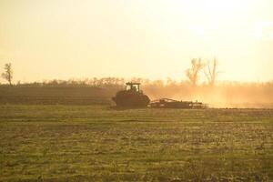 tractor a puesta de sol arado arado un campo. labranza el suelo en el otoño después cosecha. el final de el temporada foto