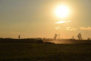 Tractor at sunset plow plow a field. Tilling the soil in the fall after harvest. The end of the season photo