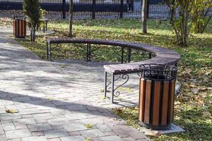 bench in an autumn park. Pavement of tiles and garbage can. photo