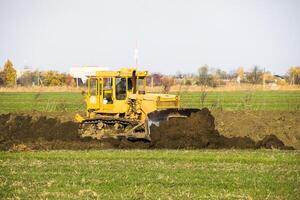 el amarillo tractor con adjunto grederom hace suelo arrasamiento. foto