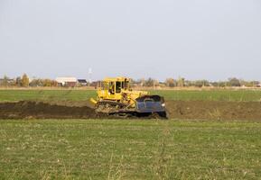 The yellow tractor with attached grederom makes ground leveling. photo