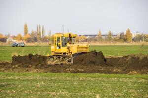 The yellow tractor with attached grederom makes ground leveling. photo